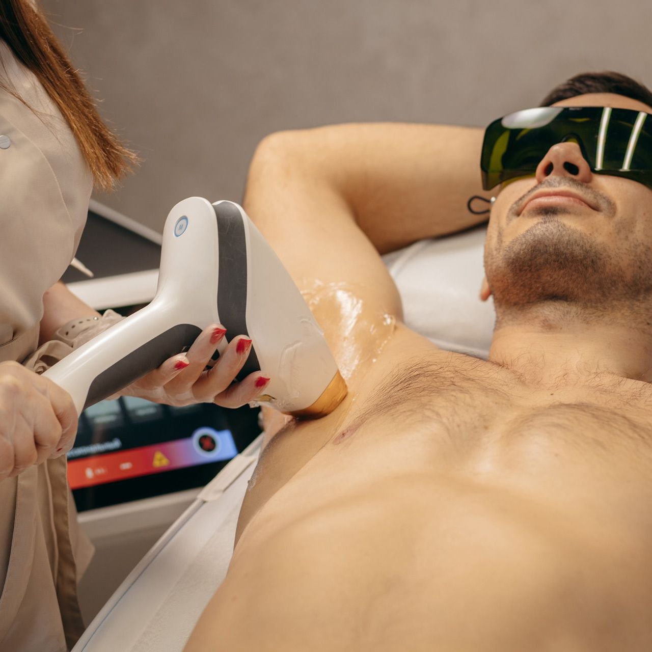 Laser hair removal on a reclining man wearing protective goggles in a spa treatment room